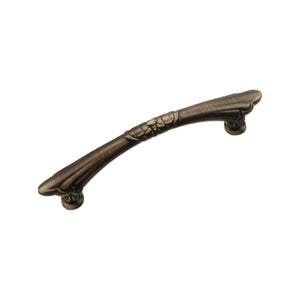 Aged bronze-tone curved bar pull with ring bands at the center and tapered ends, 96 mm.