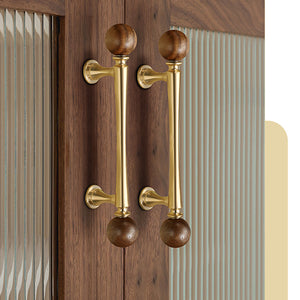 Brass bar cabinet pulls with dark wood ball ends installed on wood cabinet doors.