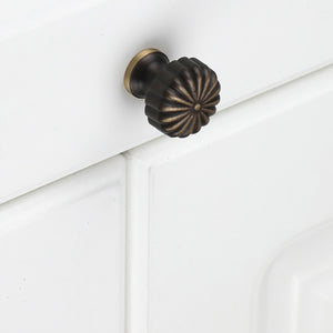 Fluted bronze-finish brass knob installed on a white cabinet drawer.