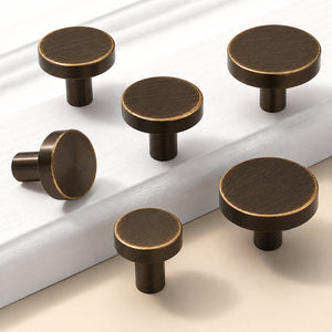 Five flat round bronze-finish brass cabinet knobs in assorted sizes.