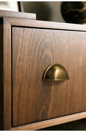 Solid brass open-back cup pull in Antique Brass on a wood-grain cabinet front, viewed at an angle.