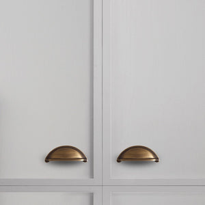 Solid brass open-back cup pulls in Antique Brass on white paneled cabinet doors.