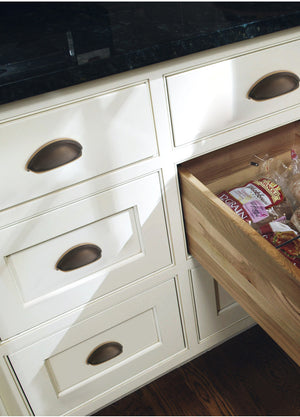 Solid brass open-back cup pulls in Antique Bronze on cream kitchen drawers, with one drawer open.