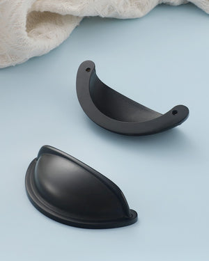 Front and back views of the solid brass open-back cup pull in Matte Black, showing its curved face and two mounting holes.