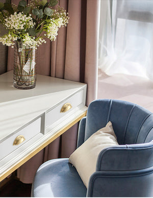 Solid brass open-back cup pulls in Polished Gold shown on white drawers beside a blue chair.