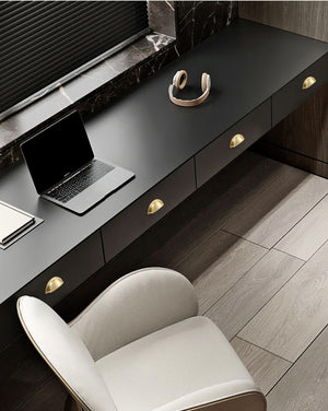 Solid brass open-back cup pulls in Satin Brass on the drawers of a dark desk.