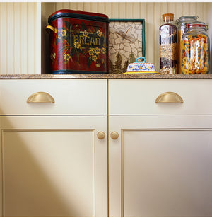 Solid brass open-back cup pulls in Satin Brass on cream kitchen drawers.