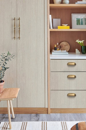 Solid brass rounded dome cup pulls in Aged Brass on light wood-grain drawers beside a tall cabinet.