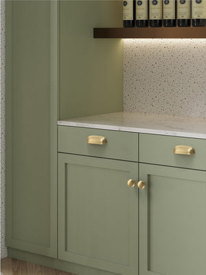 Solid brass rounded dome cup pulls in Satin Brass on green cabinet drawers.