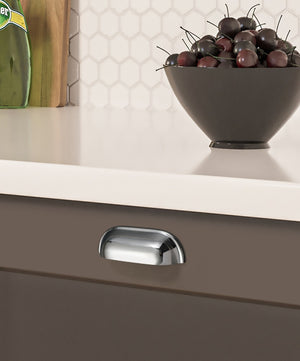Solid brass soft-corner cup pull in Polished Chrome on a dark kitchen drawer beneath a white countertop.