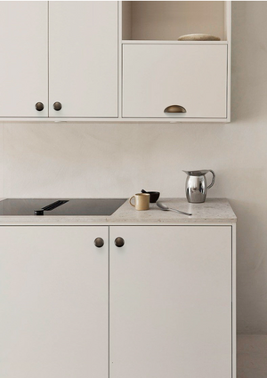 Antique bronze half-moon cup pull on a white kitchen cabinet front above the countertop.