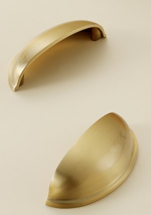 Two satin brass half-moon cup pulls showing the curved face and underside.