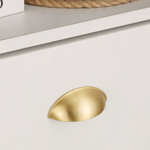 Satin brass half-moon cup pull mounted on a white drawer, close-up.