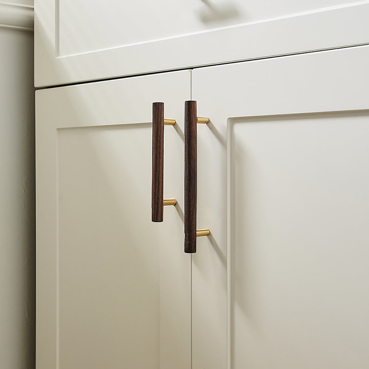 Walnut wood bar cabinet pulls with brass mounts installed on white cabinet doors.