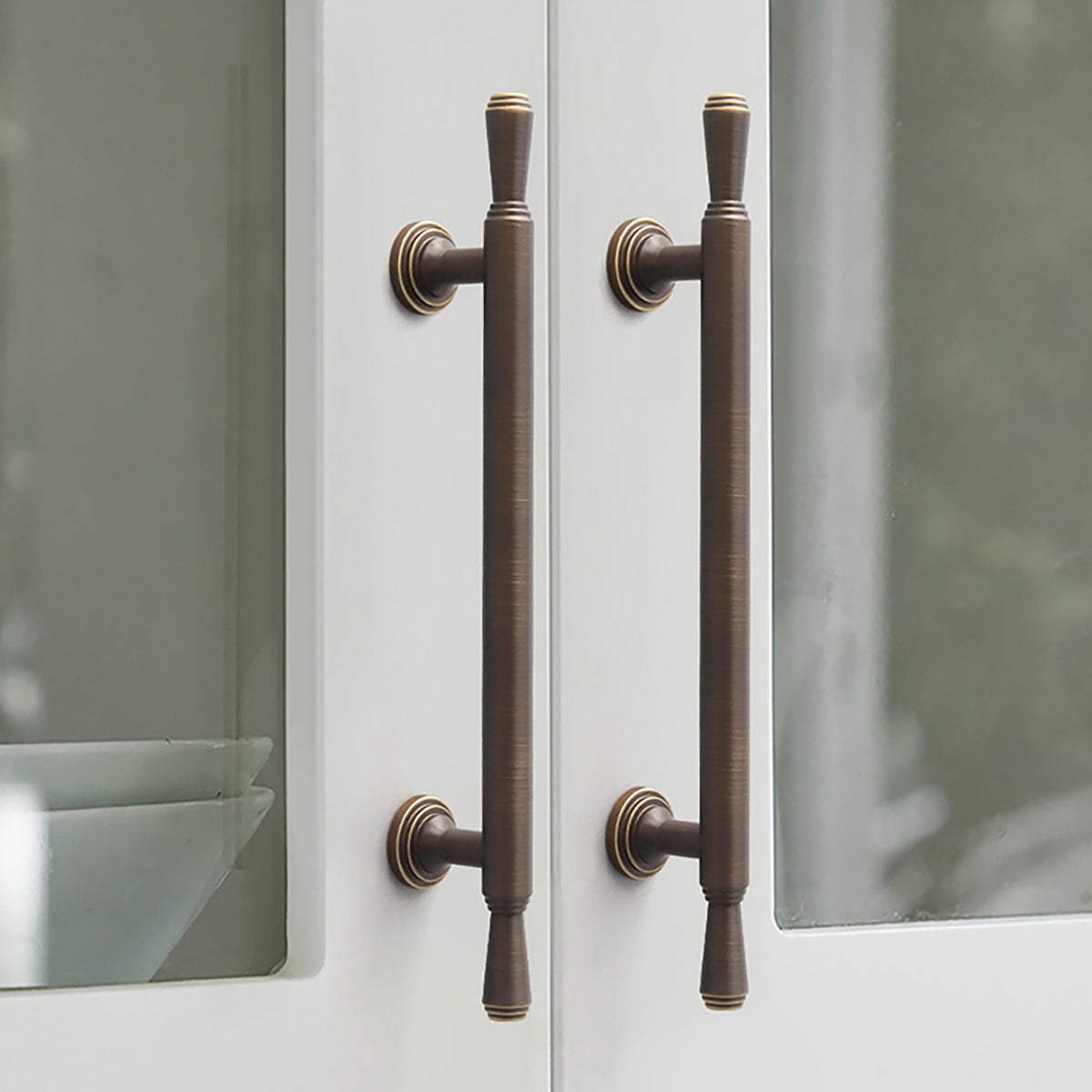 Pair of dark antique brass bar cabinet pulls installed on white doors with glass panels.