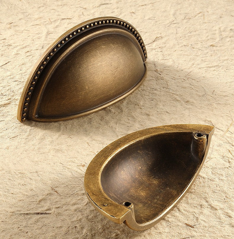 Front and rear views of the solid brass beaded-rim half-moon cup pull in Antique Brass, showing the decorative rim and mounting posts.