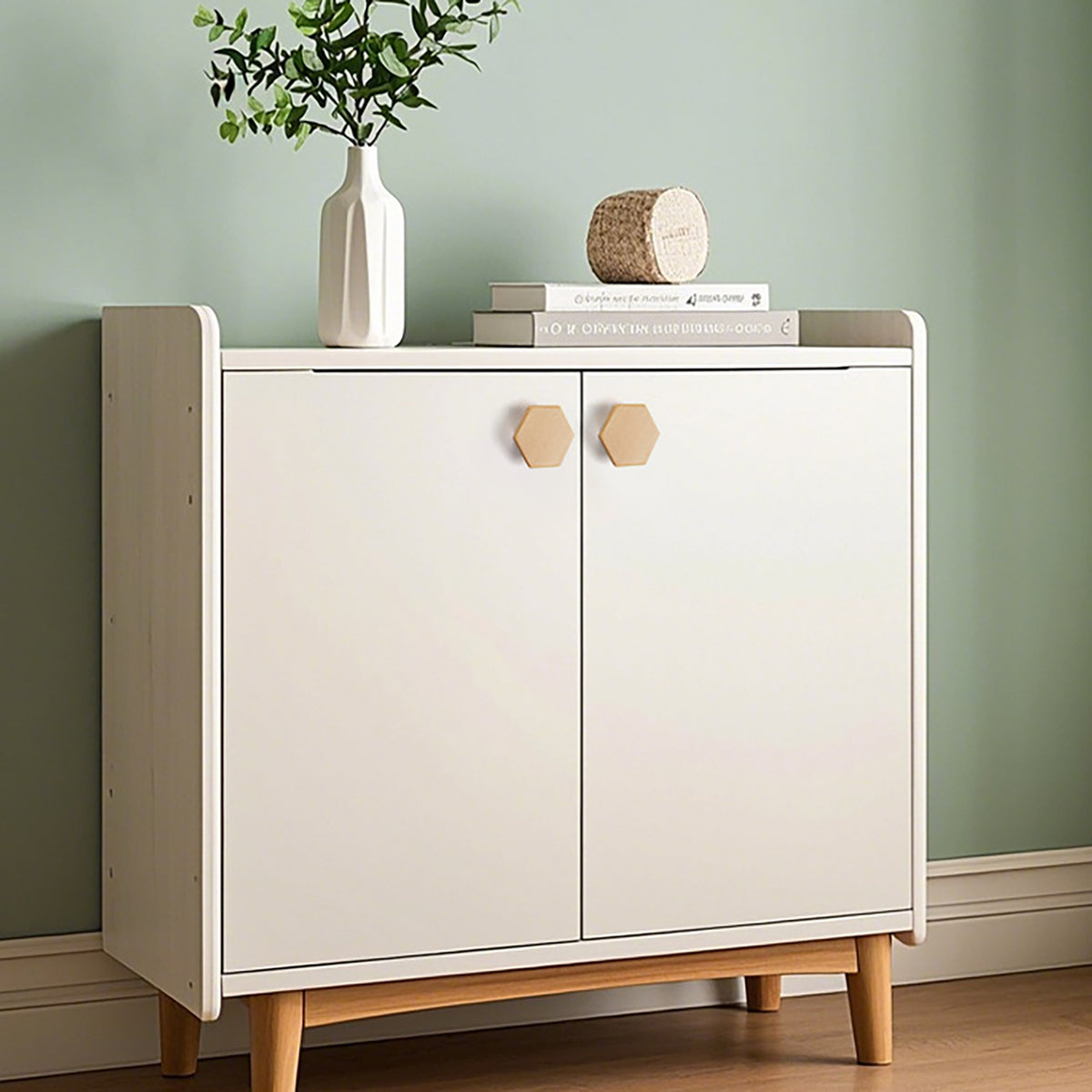 Two faceted beech wood cabinet knobs on a white cabinet against a green wall.