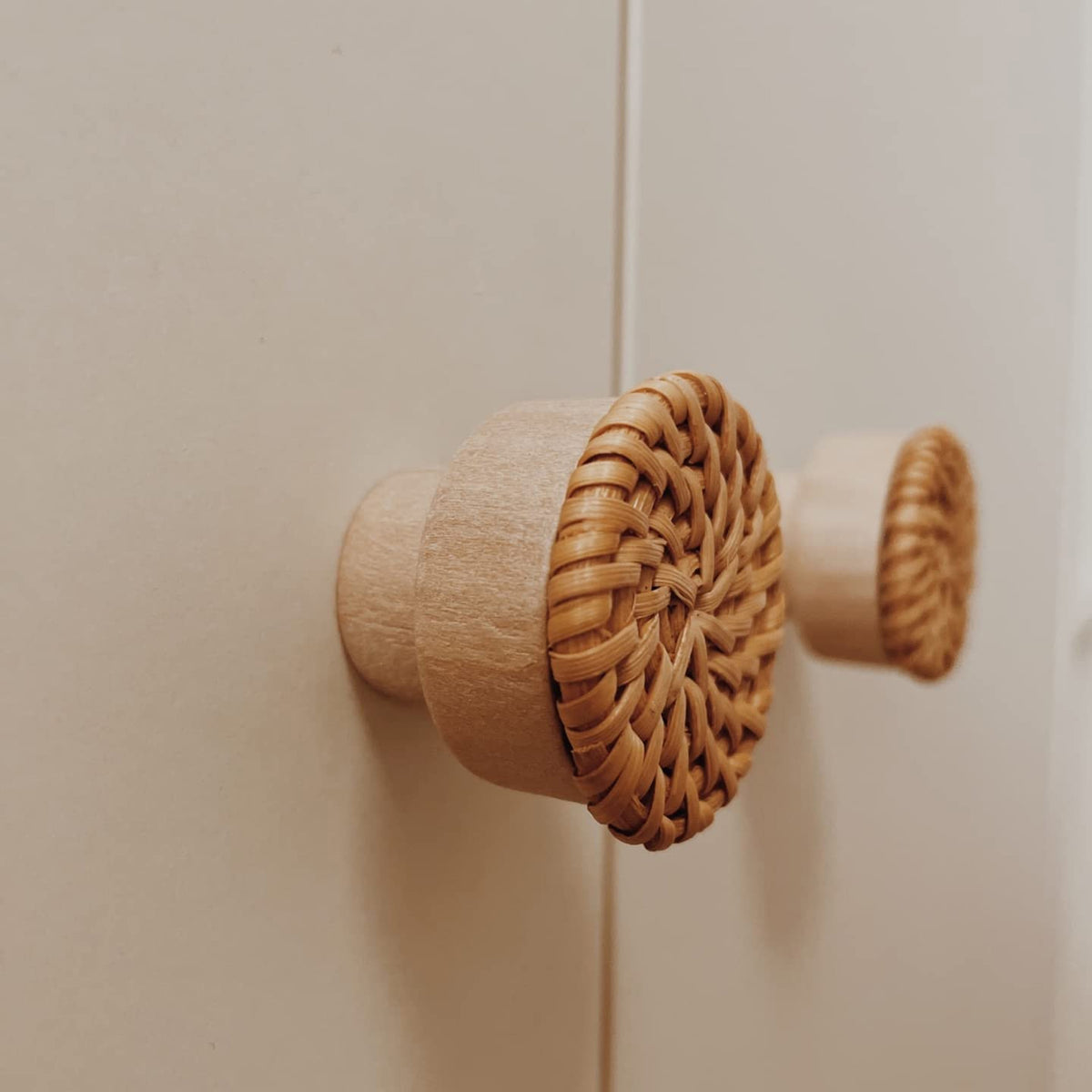 Woven rattan-topped wood cabinet knob installed on a light cabinet door.
