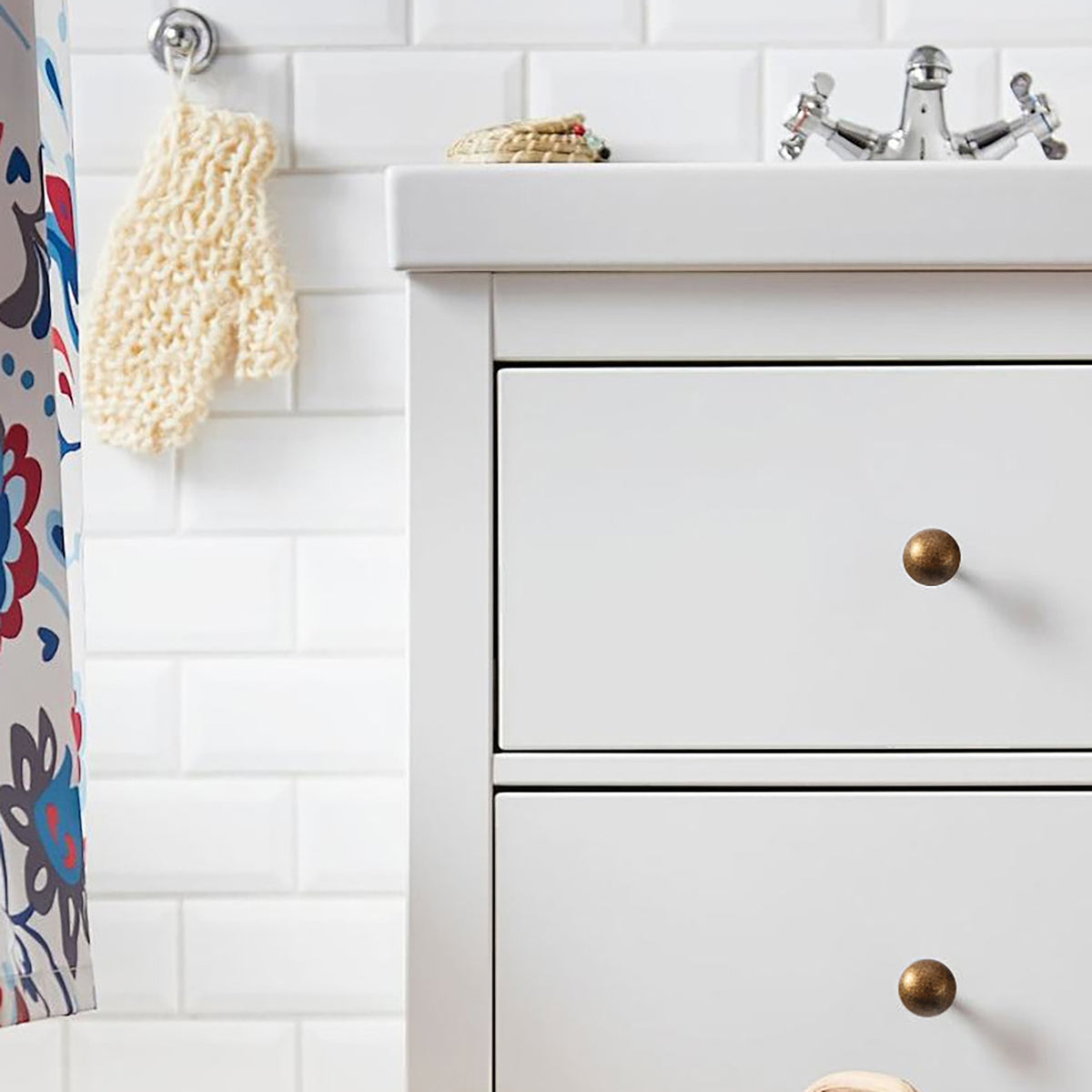 Round bronze-finish brass knobs installed on white bathroom drawers.