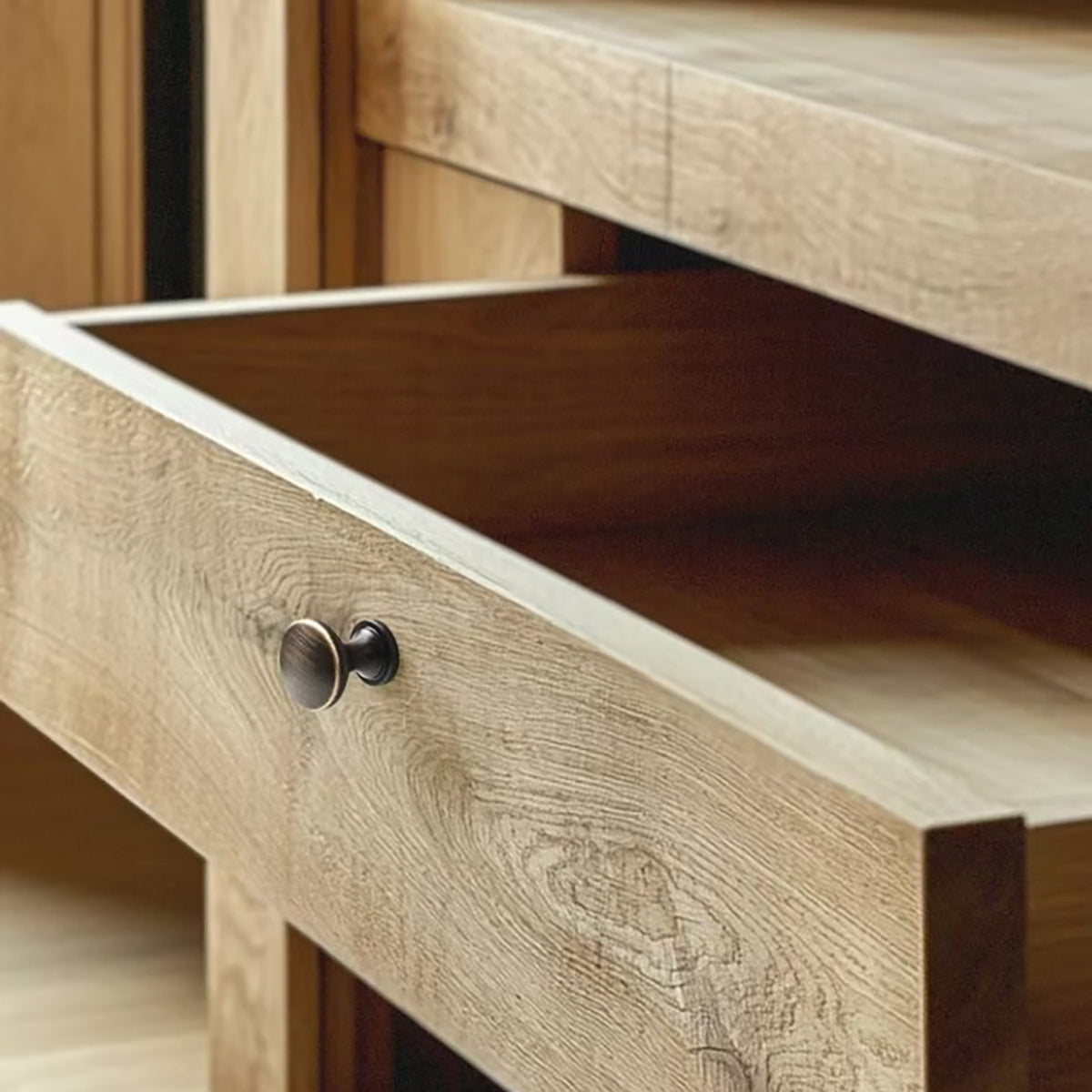 Bronze-finish round cabinet knob installed on an open wood drawer.