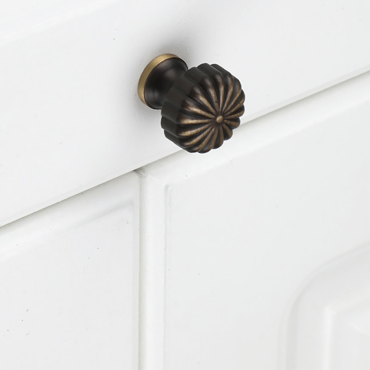 Fluted bronze-finish brass knob installed on a white cabinet drawer.