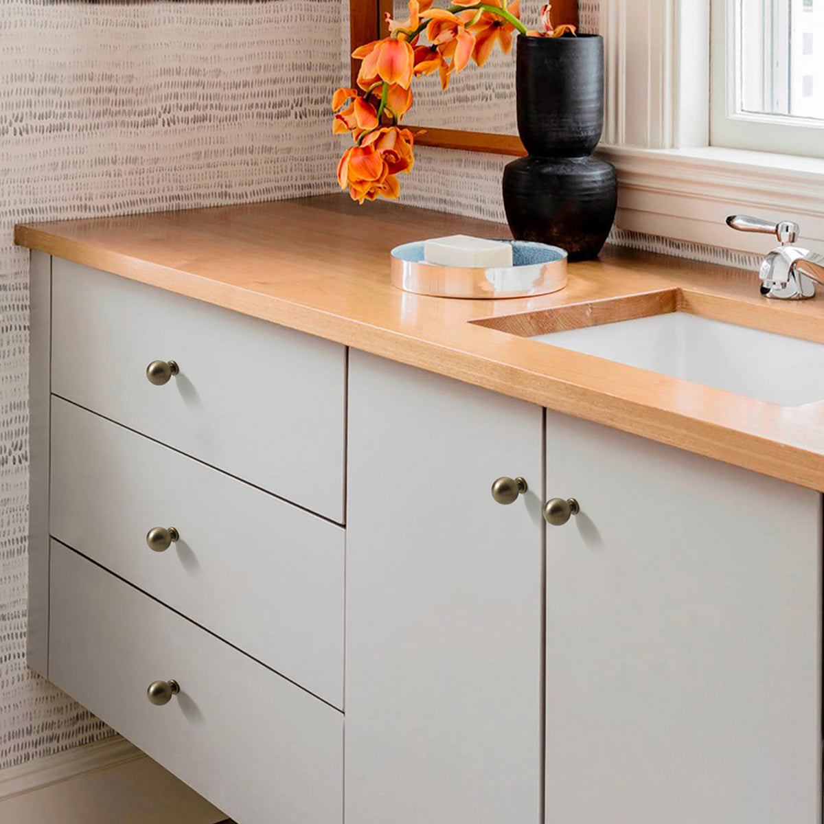 Round bronze-finish brass knobs installed on a gray kitchen cabinet.