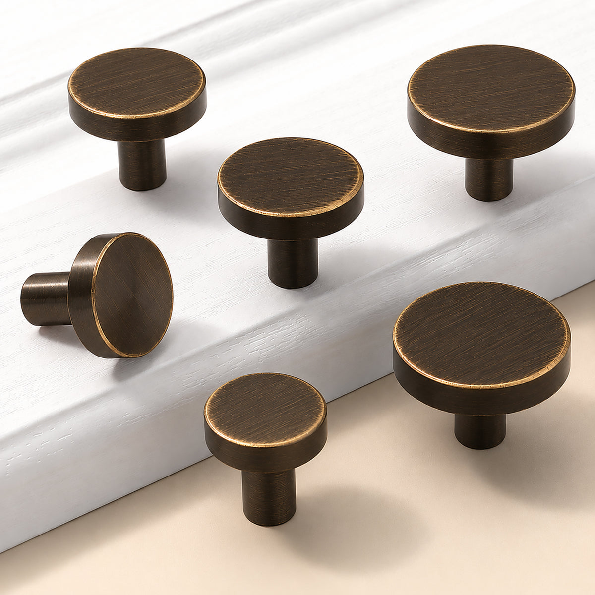 Five flat round bronze-finish brass cabinet knobs in assorted sizes.
