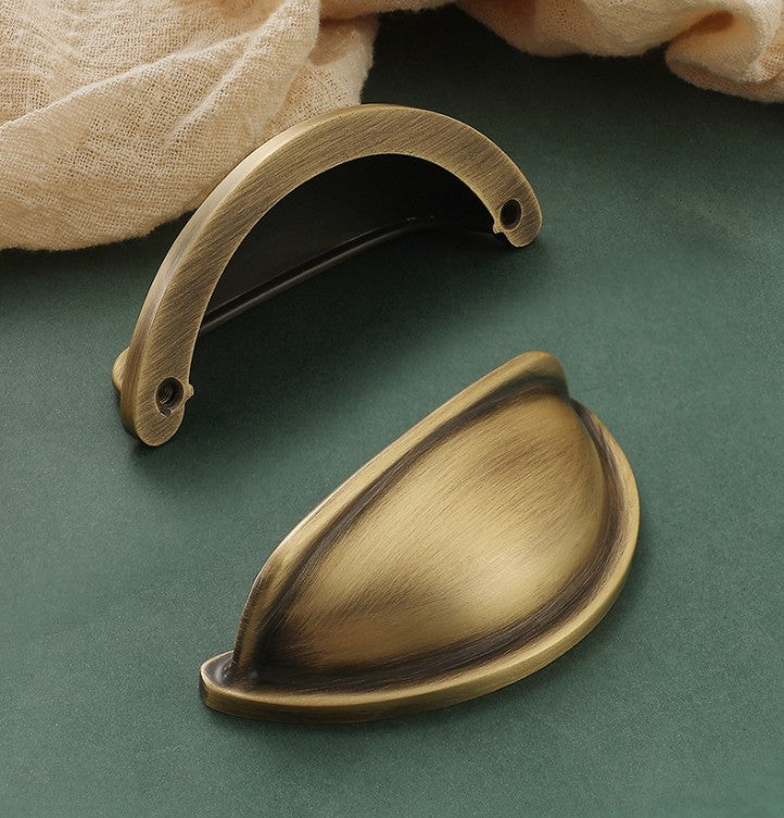 Front and rear views of the solid brass open-back cup pull in Aged Brass, showing two rear mounting holes.