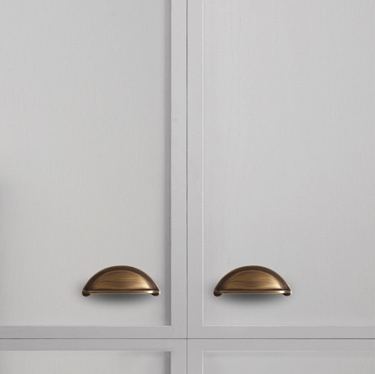 Solid brass open-back cup pulls in Antique Brass on white paneled cabinet doors.