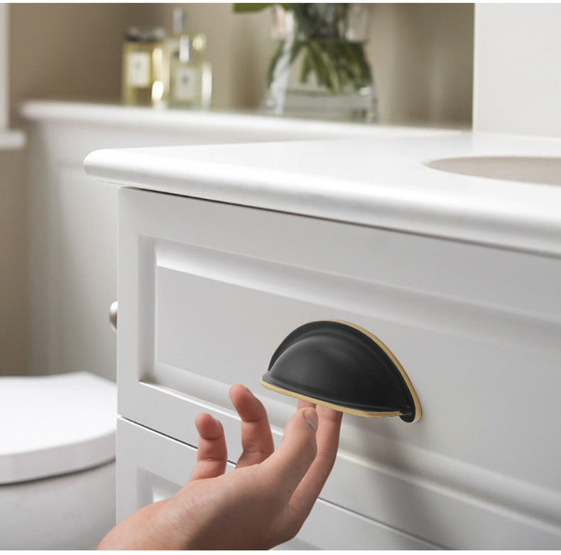 Solid brass open-back cup pull in Blackened Bronze shown on a white bathroom cabinet, with a hand beneath the grip.