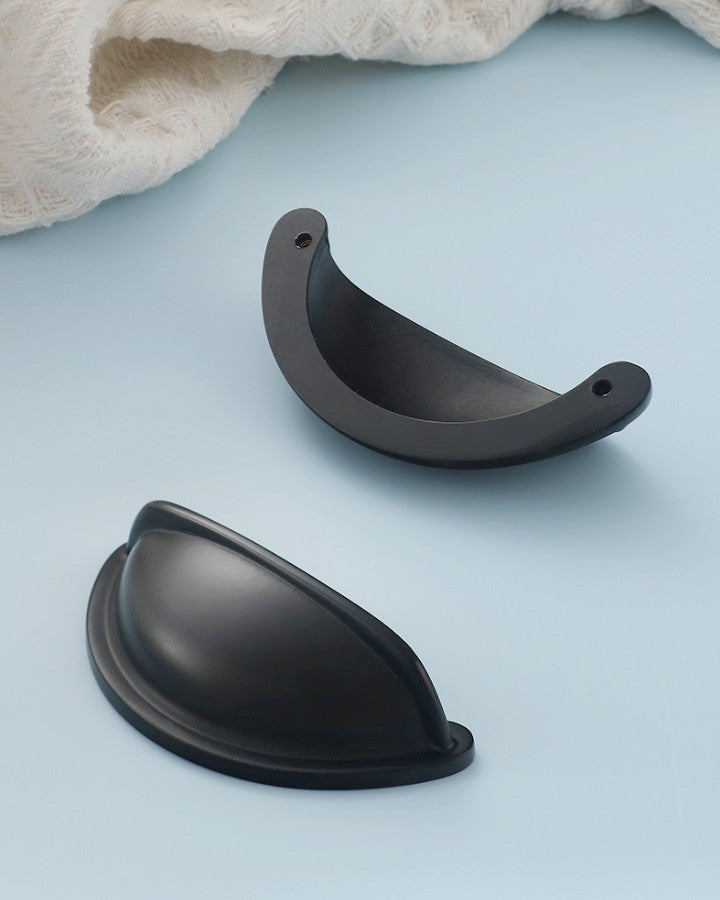 Front and back views of the solid brass open-back cup pull in Matte Black, showing its curved face and two mounting holes.