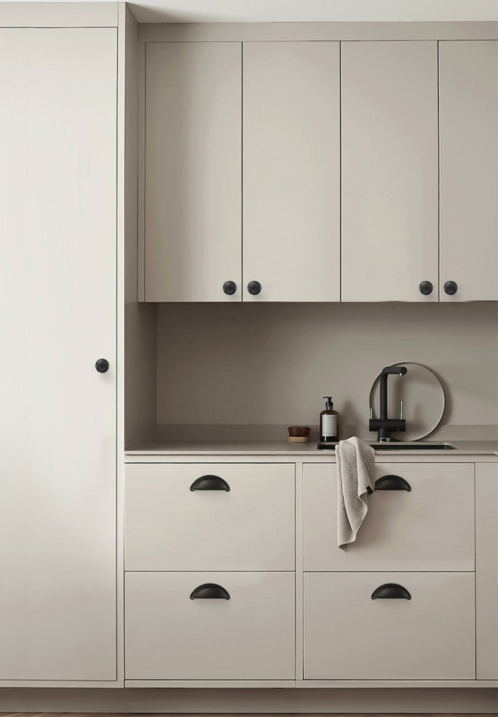 Solid brass open-back cup pulls in Matte Black shown on light kitchen drawers beneath a sink.