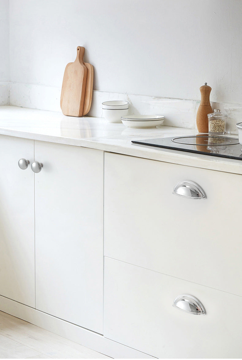 Solid brass open-back cup pulls in Polished Chrome shown on white kitchen drawers beside a cooktop.