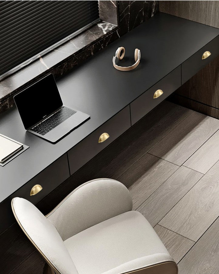 Solid brass open-back cup pulls in Satin Brass on the drawers of a dark desk.