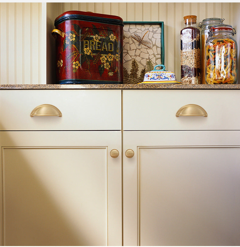 Solid brass open-back cup pulls in Satin Brass on cream kitchen drawers.