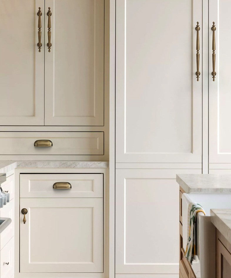 Solid brass ribbed-rim arch cup pulls in Aged Brass on cream kitchen drawers.