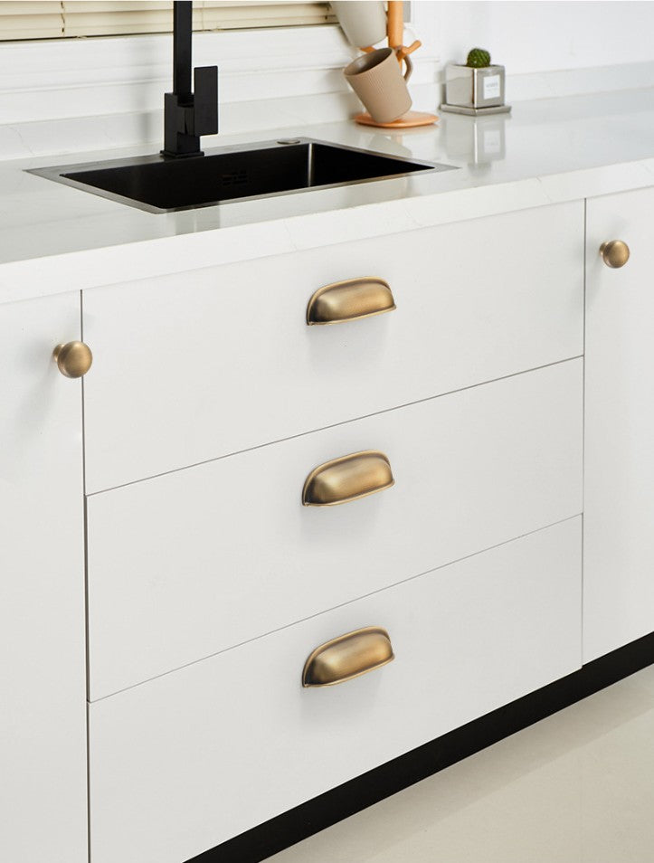 Solid brass rounded dome cup pulls in Burnished Brass on white kitchen drawers beneath a sink.
