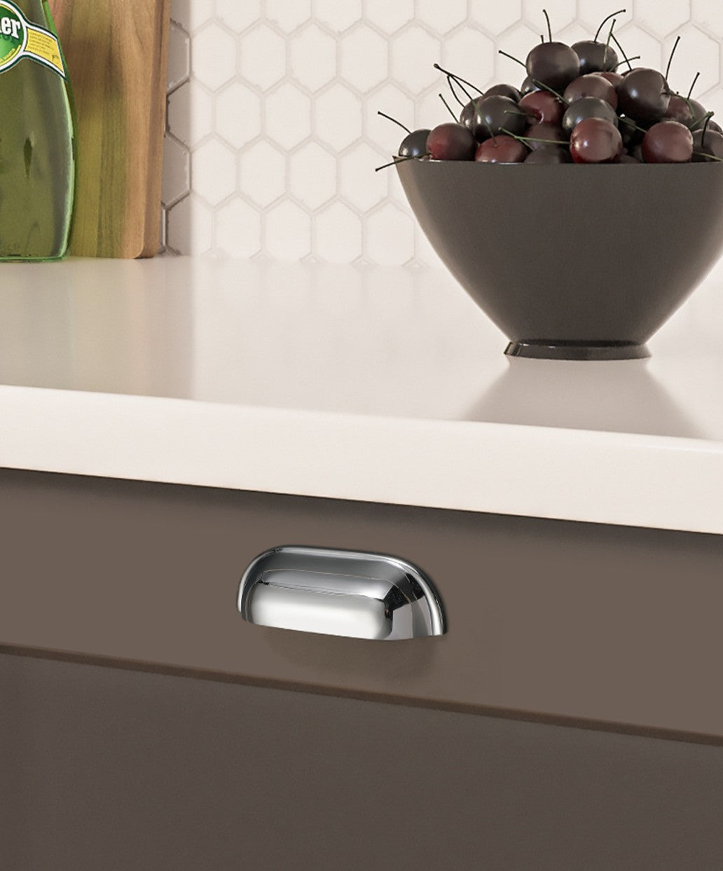 Solid brass soft-corner cup pull in Polished Chrome on a dark kitchen drawer beneath a white countertop.