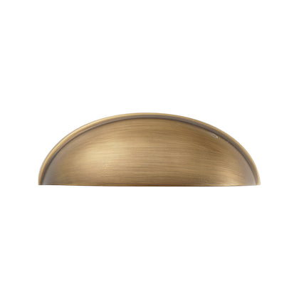 Solid brass half-moon cup pull in aged brass, front view on white.