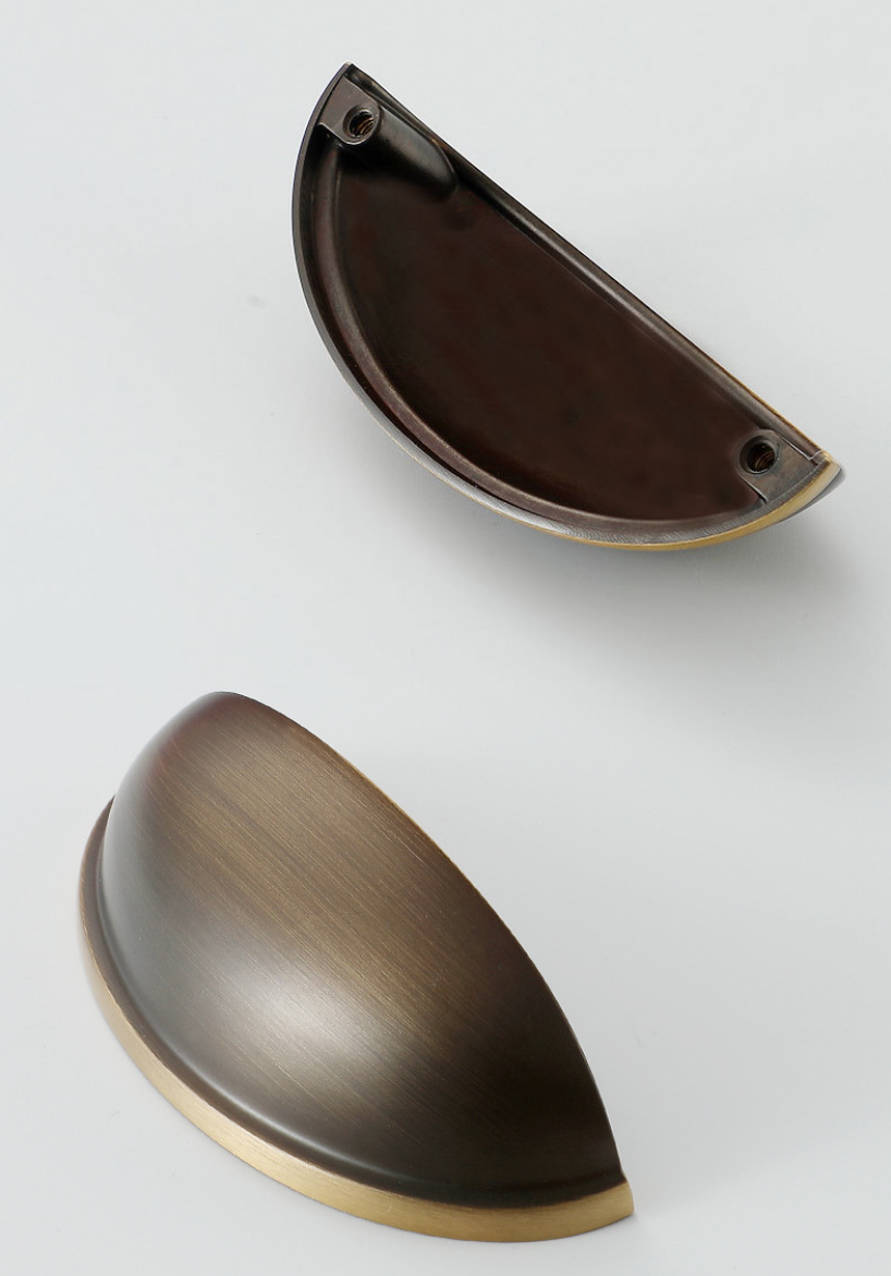 Two antique bronze half-moon cup pulls showing the front, brass-toned rim, and underside with mounting holes.