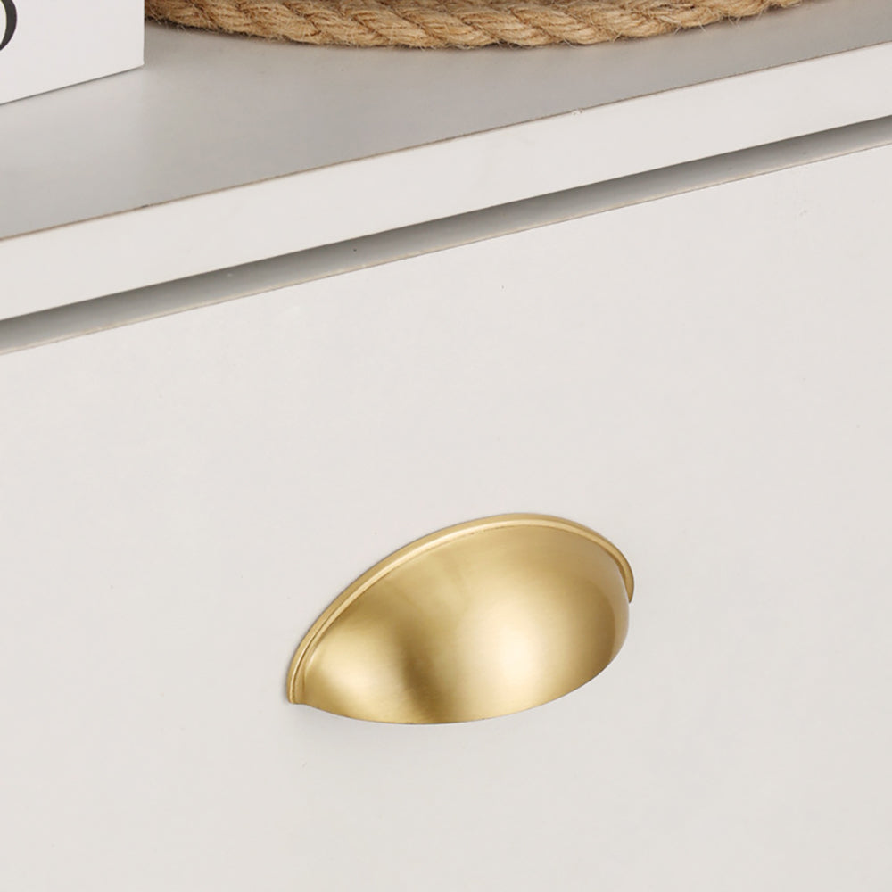 Satin brass half-moon cup pull mounted on a white drawer, close-up.